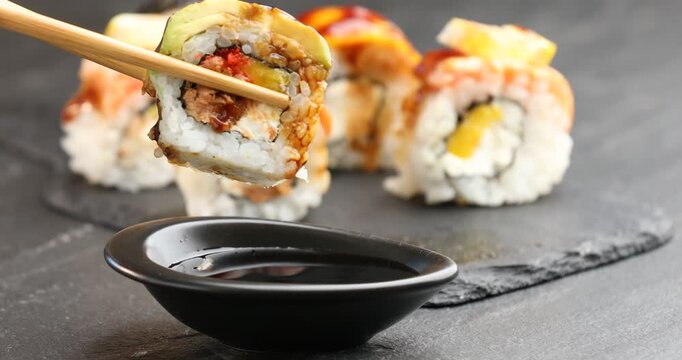 Woman dipping tasty sushi roll into soy sauce at black table, closeup