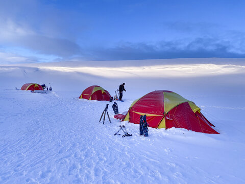 Dovre Municipality, Innlandet, Norway - 19 February 2020: View of red and yellow tents set up in the snowy landscape of Dovrefjell with people and winter equipment.