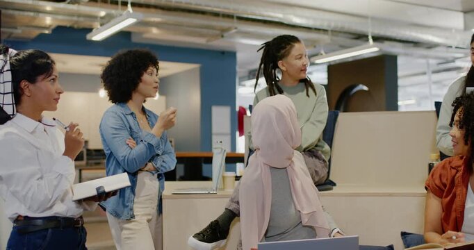 Diverse team on tiers, standing pen-gesturing speaker, pink hijab woman using laptop, planning