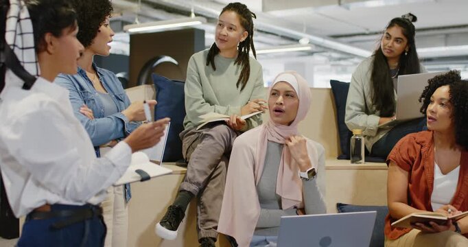 Team at office meeting watching presenter gesturing, others noting, hijab woman preparing laptop