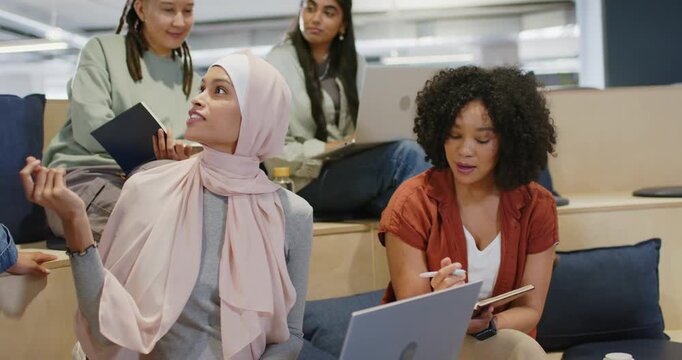 Diverse team collaborating on tiers, hijab speaker gesturing with silver laptop as person entering
