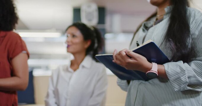 Diverse coworkers standing in open office, responding to meeting prompt, holding laptops, notebooks