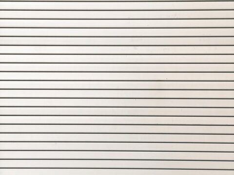 White corrugated metal shutter texture with parallel horizontal lines, close-up view of ribbed industrial surface pattern.
