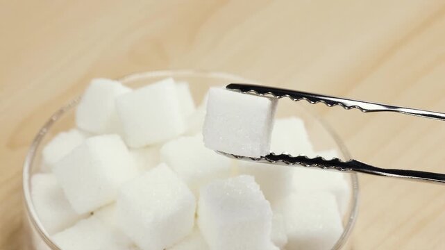Picking Up White Sugar Cube with Metal Tongs from Glass Bowl