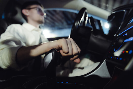 A portrait of a young man behind the wheel, with his hand on the gear shift while driving.