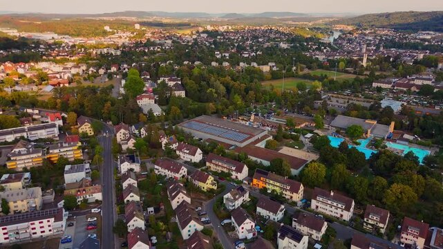 Aerial view of Schaffhausen, Switzerland, with IWC Arena and rooftop solar panels among residential neighborhoods, public pools and wooded hills in warm evening light.