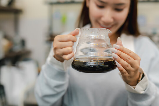 Smiling female barista holding glass server of freshly brewed pour over coffee at cafe, presenting handcrafted black coffee after manual brewing for professional beverage service.
