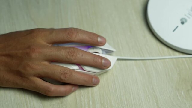 Hand using wired mouse beside wireless router, Close-up of a hand using a wired computer mouse on a light wood desk beside a wireless router, showing everyday online work and internet connection.
