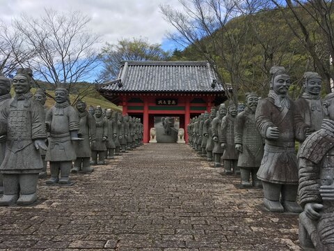日本の伝統的な門へと続く石畳の参道と並ぶ兵士の石像