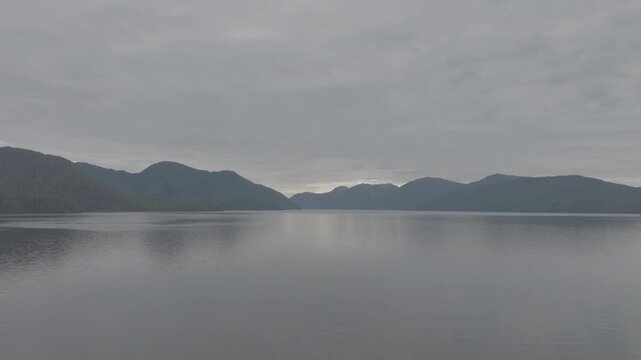 Aerial view of mirror calm water and layered mountain ridges in a coastal fjord at dawn &mdash; distant mountains through haze