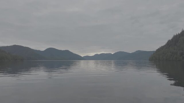 Aerial view of mirror calm water and layered mountain ridges in a coastal fjord at dawn &mdash; layered ridges in soft light