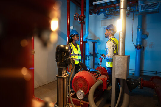 Standby pump set checked against the maintenance record while she points out the pressure gauge on the pump, beside the horizontal pump and motor on its plinth.