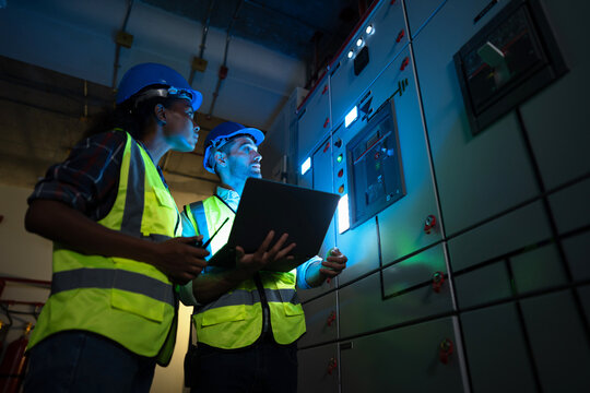 Power distribution inspection by a two person team as a reading is confirmed between the two of them, in the low light of a medium voltage switch room. A facilities management walkdown.