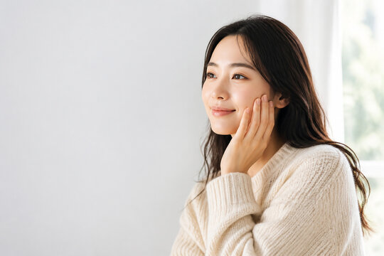 笑顔で肌に触れるセーター姿の女性