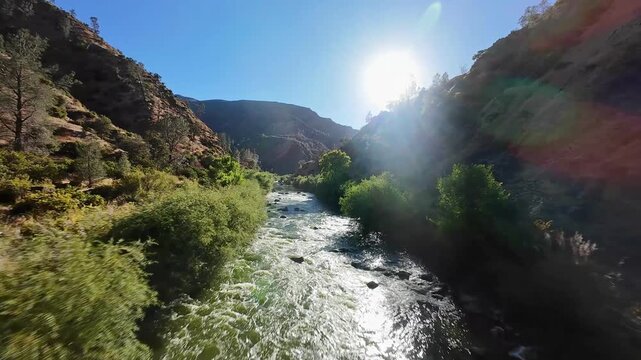 FPV drone shot flying fast over the clear green water of Cache Creek, California, with the bright sun reflecting on the surface and lighting up the lush canyon landscape