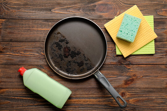 Kitchen cleaning and household chores, dirty burnt frying pan with dish soap and sponges on wooden table for home maintenance and housekeeping tasks