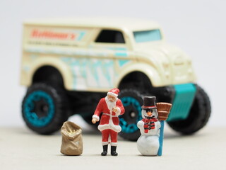 Mini toy of action figure at table with blurred background. Miniature photography concept design. Minifigure of santa claus character and snowman with monster truck. Big car at snow land. Xmas party. © awstoys