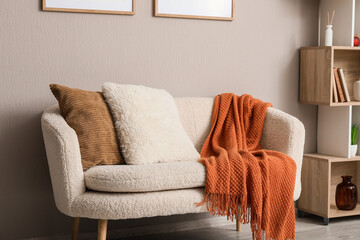 Hygge home interior and cozy living room decor, soft cream sofa with textured pillows and warm orange throw blanket in a modern apartment setting © Pixel-Shot