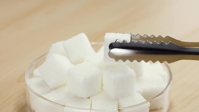Metal Tongs Picking Up White Sugar Cube from Glass Bowl