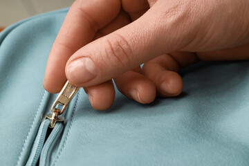 Organization and preparation, hand pulling a zipper on a blue leather bag to open or close personal belongings for travel or daily commute © Pixel-Shot