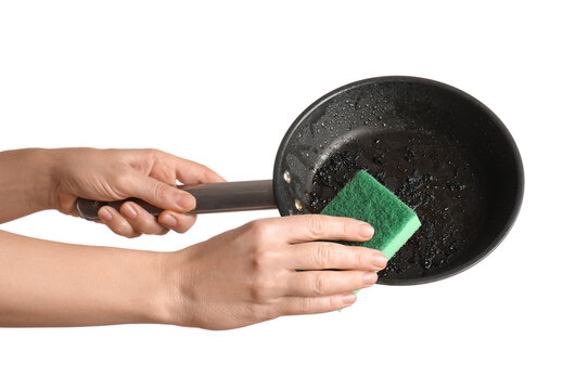 Housework and kitchen hygiene, person scrubbing a burnt frying pan with a green sponge to remove grease and food residue on a white background