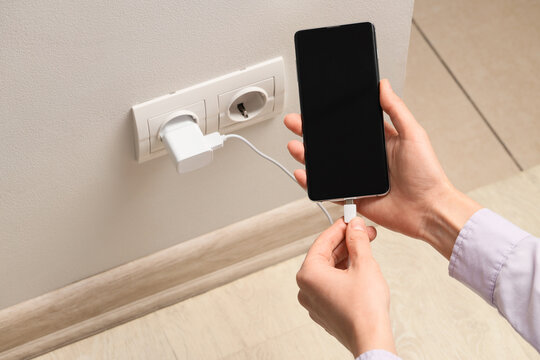 Battery charging and mobile connectivity, person plugging smartphone into wall outlet for power supply and energy management in modern home interior