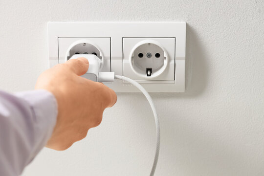 Energy consumption and power supply, hand plugging a charger into a wall outlet for electronic device charging and electricity usage in modern home