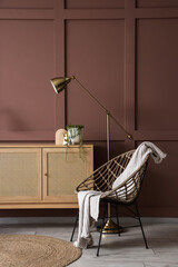 Plakat Chest of drawers, armchair and lamp near brown wall in interior of living room, closeup