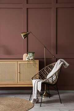 Chest of drawers, armchair and lamp near brown wall in interior of living room, closeup
