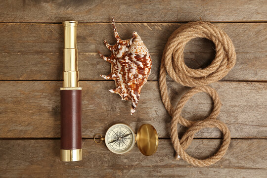 Composition with golden compass, rope, spyglass and seashell on wooden background