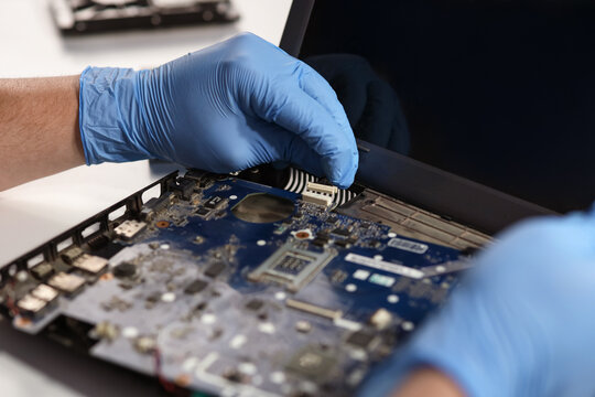 Male technician repairing laptop on table in service center, closeup