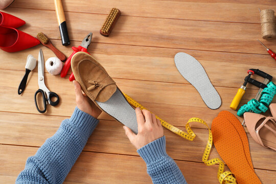 Mature shoemaker putting insole into shoe at table in workshop, top view
