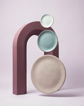 Modern minimalist composition featuring three stacked ceramic plates balanced against a sculptural purple arch on a soft pastel background