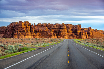 Fototapeta premium Sunrise illuminates scenic road toward sandstone cliffs near Goblin Valley