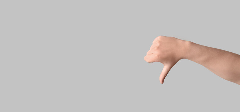 Disapproval and rejection concept, human hand showing thumbs down gesture to express negative feedback or bad service on a plain gray background