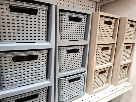close-up view of modular plastic storage drawers and woven-texture organizer baskets displayed on store shelves in grey and beige colors.