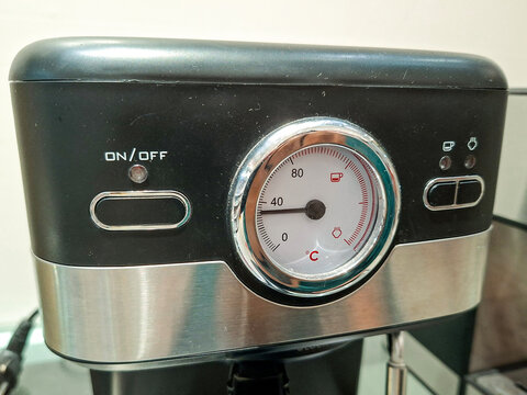 close-up view of the front control panel of a black and stainless steel coffee espresso machine featuring an analog temperature gauge and power button.