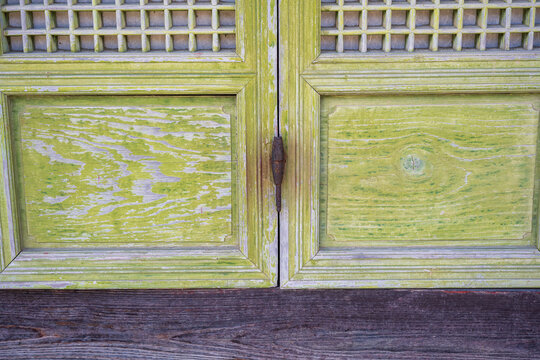 Traditional wooden latticed door with weathered green panels and iron latch on buddhist temple building in South Korea.