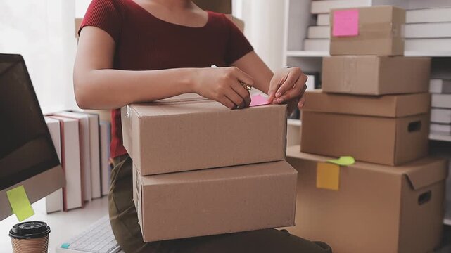 Startup SME small business entrepreneur of freelance Asian woman wearing apron using laptop and box to receive and review orders online to prepare to pack sell to customers, online sme business ideas.