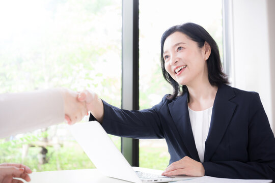 笑顔で握手をする日本人ミドル女性、商談や契約で相手と信頼関係を築く50代女性ビジネスパーソン