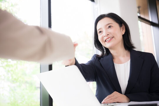 笑顔で握手をする日本人ミドル女性、商談や契約で相手と信頼関係を築く50代女性ビジネスパーソン