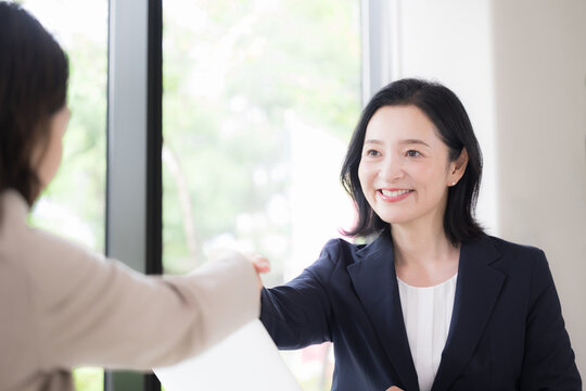 A middle-aged Japanese woman smiling as she shakes hands; a female businessperson in her 50s building trust with her counterpart during business negotiations and contract signings