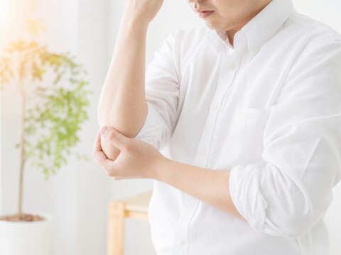 Businessman in white shirt holding sore elbow in bright office, repetitive strain injury