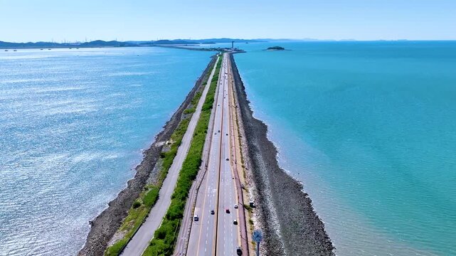 Cinematic slow-motion drone shot of cars driving along the straight sea road of Sihwa Seawall in South Korea.