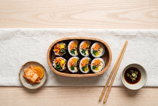 Korean Gimbap Slices in Wooden Bento Box with Kimchi, Soy Sauce, and Chopsticks Overhead