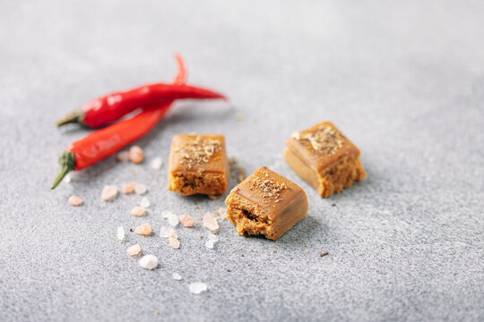 Butterscotch cubes of salted caramel with chili pepper on grey background. Trendy swicy food
