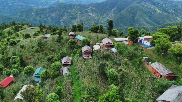 Close aerial perspective of a small cluster of rural houses perched on a grassy mountain ridge overlooking deep valleys