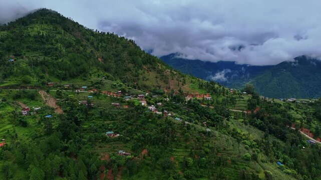 Aerial perspective of scattered rural houses and terraced agricultural fields clinging to a steep green mountainside in Nepal