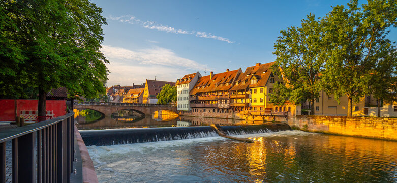 Scenic daytime view of the historic stone arch bridge spanning the calm waters of the Pegnitz River with beautiful architectural reflections in Nuremberg