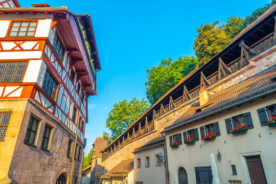 Low angle view of historic half-timbered buildings and the medieval city wall with wooden galleries and flower boxes under a bright blue sky in Nuremberg